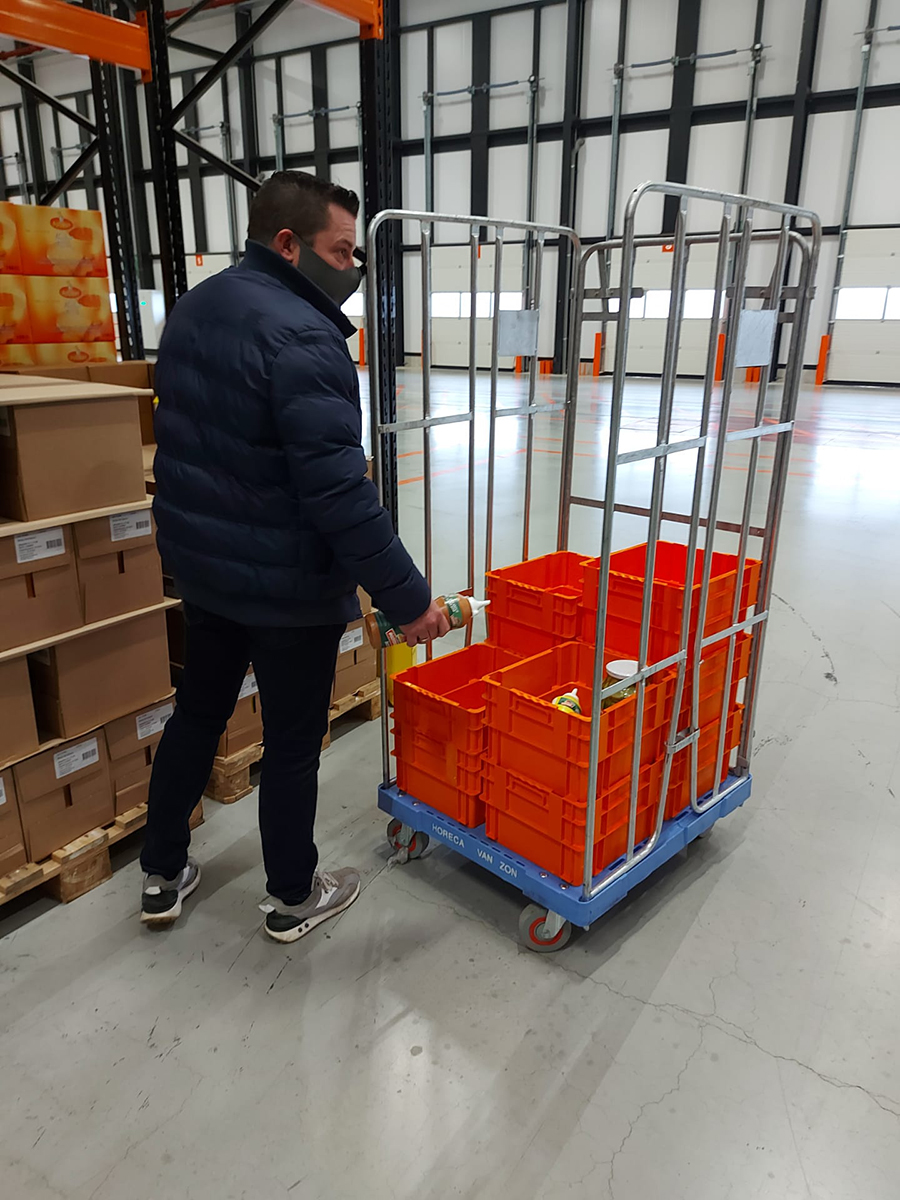 bacs gerbables rotatifs en utilisation dans l'entrepôt de Horeca Van Zon Un homme remplit les bacs empilables emboîtables avec des produits dans l'entrepôt.